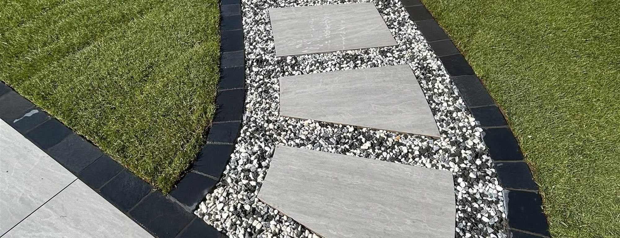 Stepping stones set into gravel curving through a bright green lawn beside a pale patio.