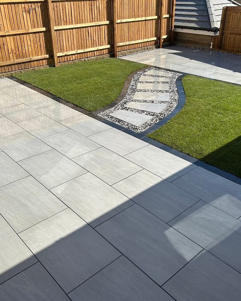 Grey porcelain patio meeting a lawn, with a stepping-stone path set into gravel.