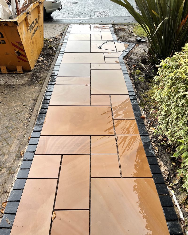 Buff Indian sandstone path edged with charcoal setts, running between planting beds.