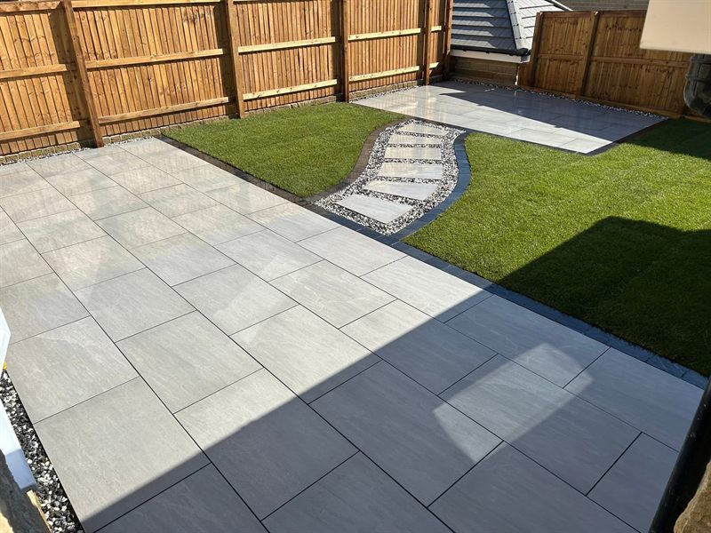 Grey porcelain patio with a stepping-stone path curving through a lawn.