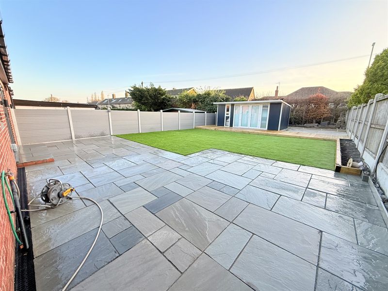 Wide Indian sandstone patio with a lawn and a garden room at the far end.