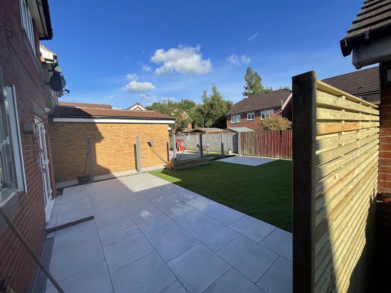 Pale patio beside a lawn under a blue sky, with a slatted timber screen to one side.