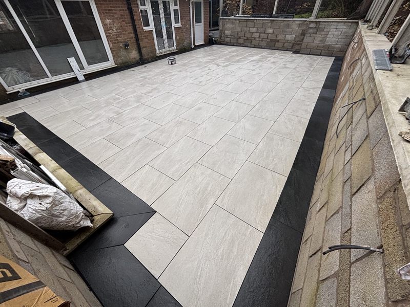 Pale grey porcelain patio with a dark border, set against a stone retaining wall.