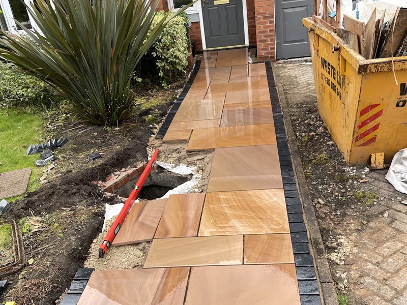 Sandstone paving part laid along a front garden with a skip on the drive.