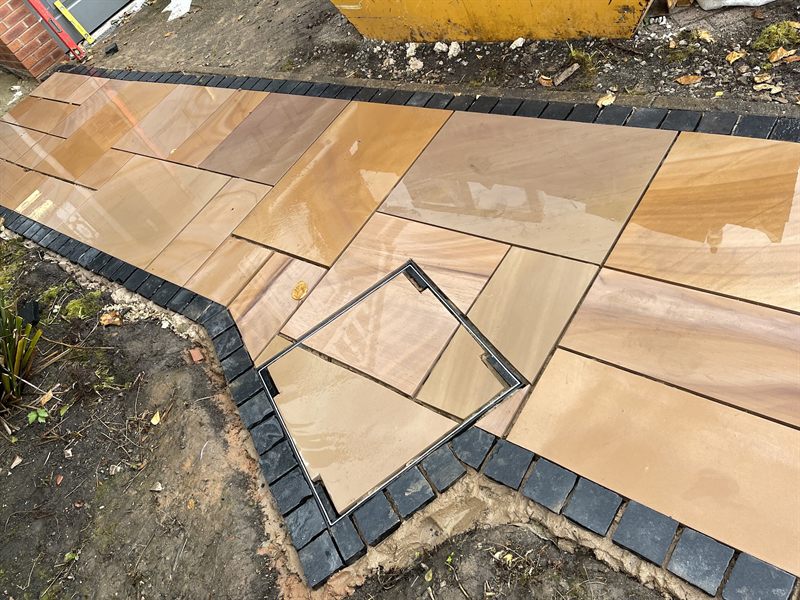 Buff sandstone slabs laid neatly around a recessed manhole cover.