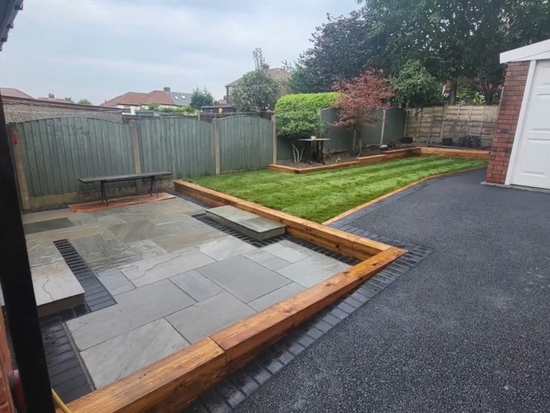 Tarmac drive beside a sandstone patio and lawn edged with new timber.