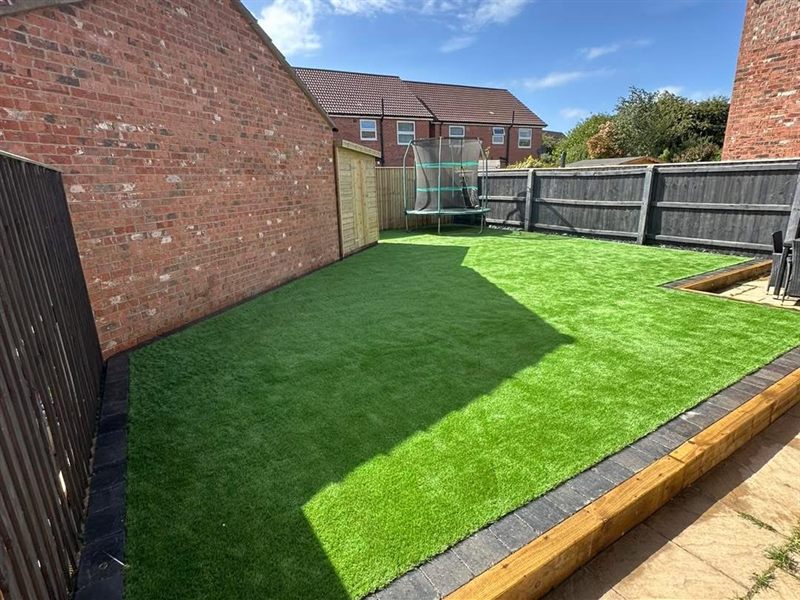 Artificial grass lawn laid to a timber edge, with a trampoline at the far end.