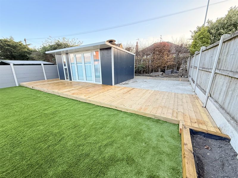 Timber deck running up to a garden room with artificial grass alongside.