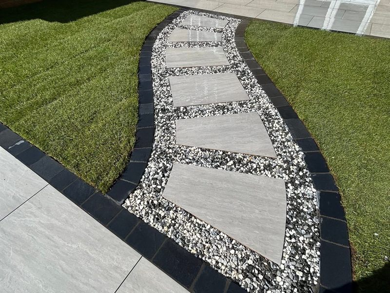 Pale stepping stones set into white gravel curving across an artificial lawn.