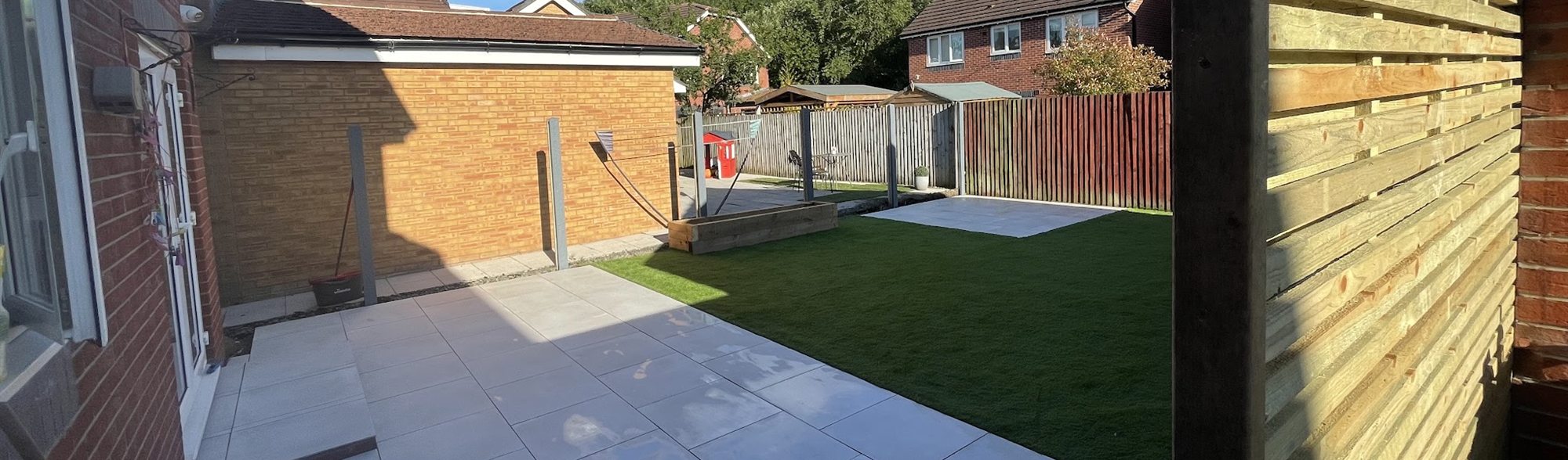 Pale grey patio with a lawn beyond it, under a clear blue sky.