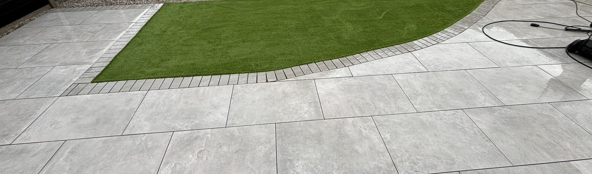 Pale grey patio curving around a lawn beside a conservatory.