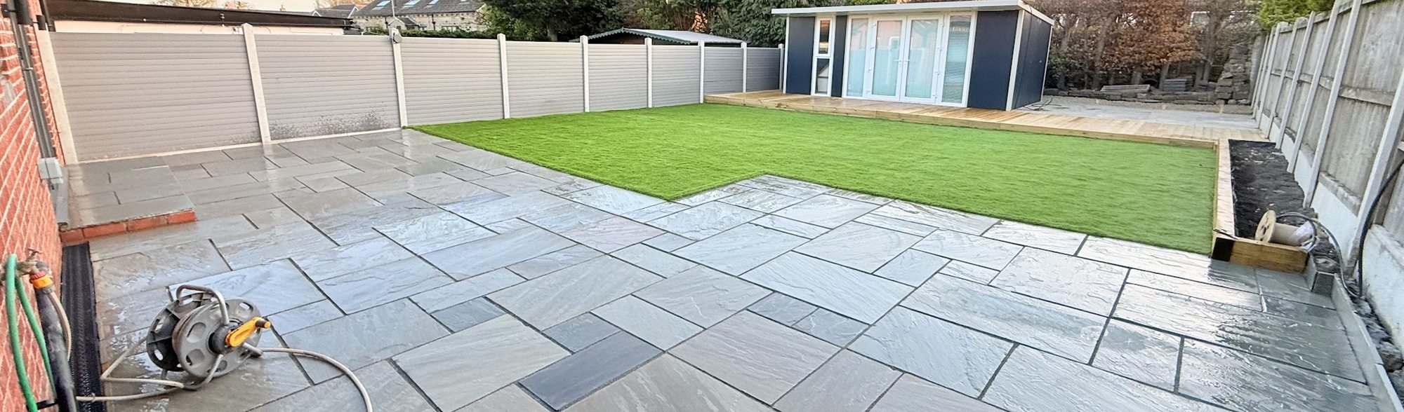 Wide Indian sandstone patio with a lawn and a garden room at the far end.