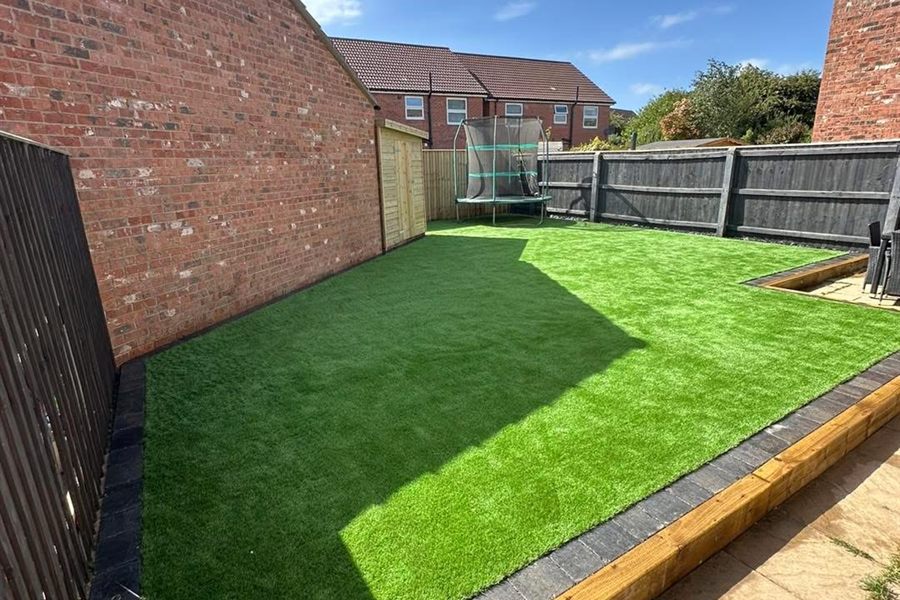Artificial grass lawn laid to a timber edge in an enclosed back garden.