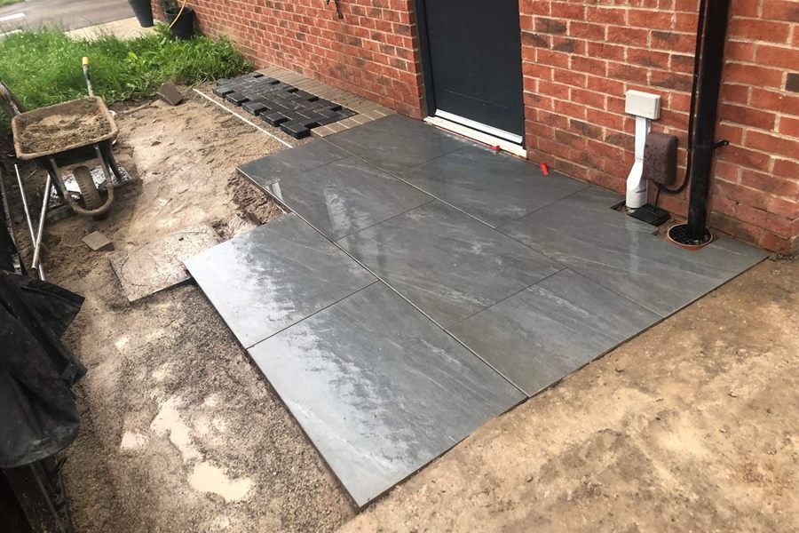 Freshly poured concrete slab beside a house wall, with a wheelbarrow to one side.