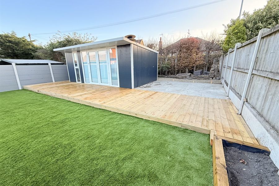 Timber deck running up to a garden room, with artificial grass alongside.
