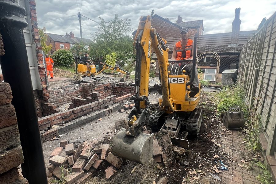 Micro digger clearing broken ground at the side of a terraced house.