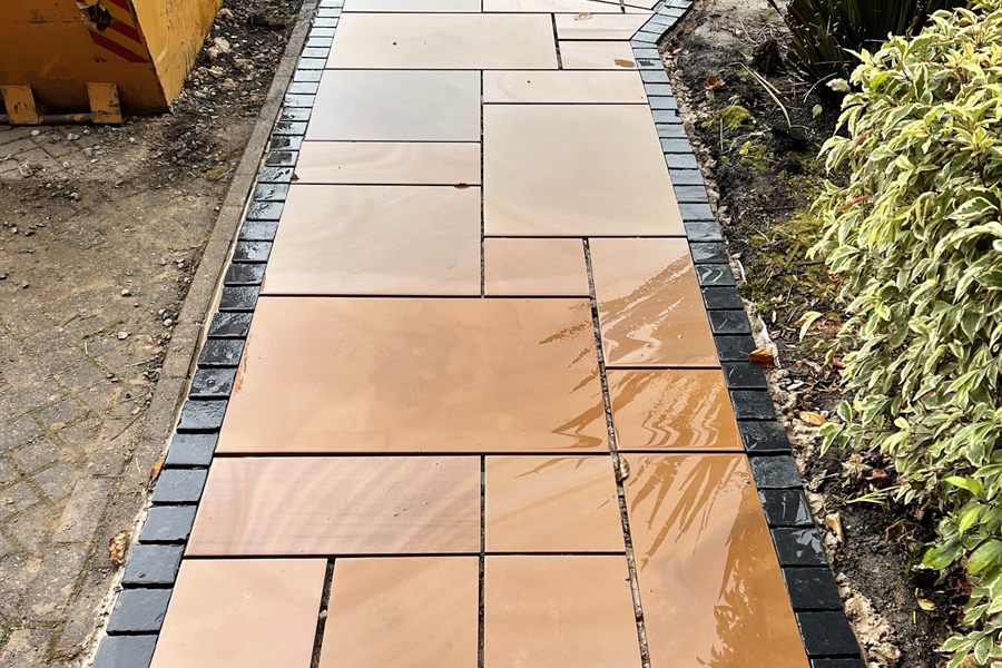 Buff Indian sandstone path edged with charcoal setts, wet from rain.