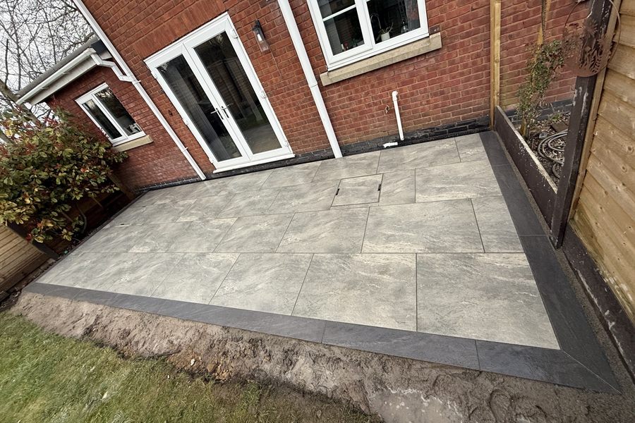 Grey porcelain patio laid with a dark contrasting border against a brick house.