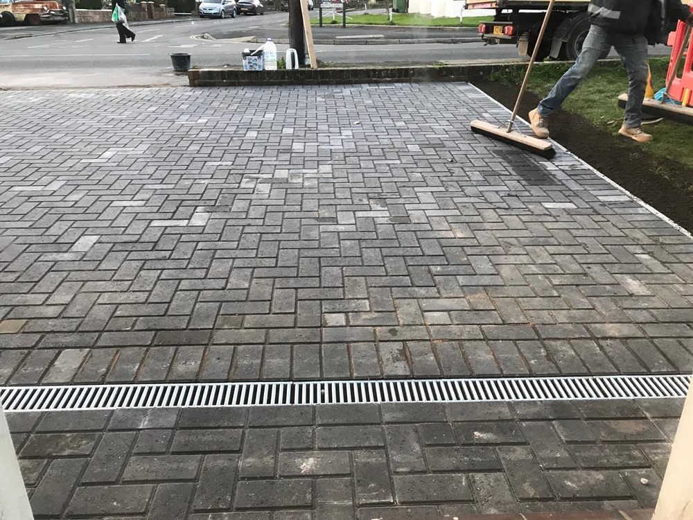 Block paving driveway being swept, with a drainage channel across the entrance.
