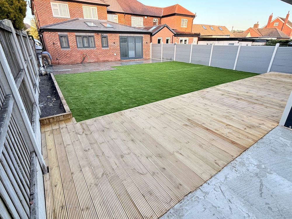 Timber decking laid along a fence line beside a lawn at the rear of a house.