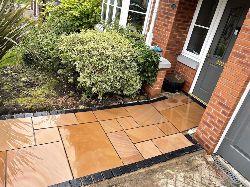 Buff Indian sandstone path laid to a front door, edged with dark setts.