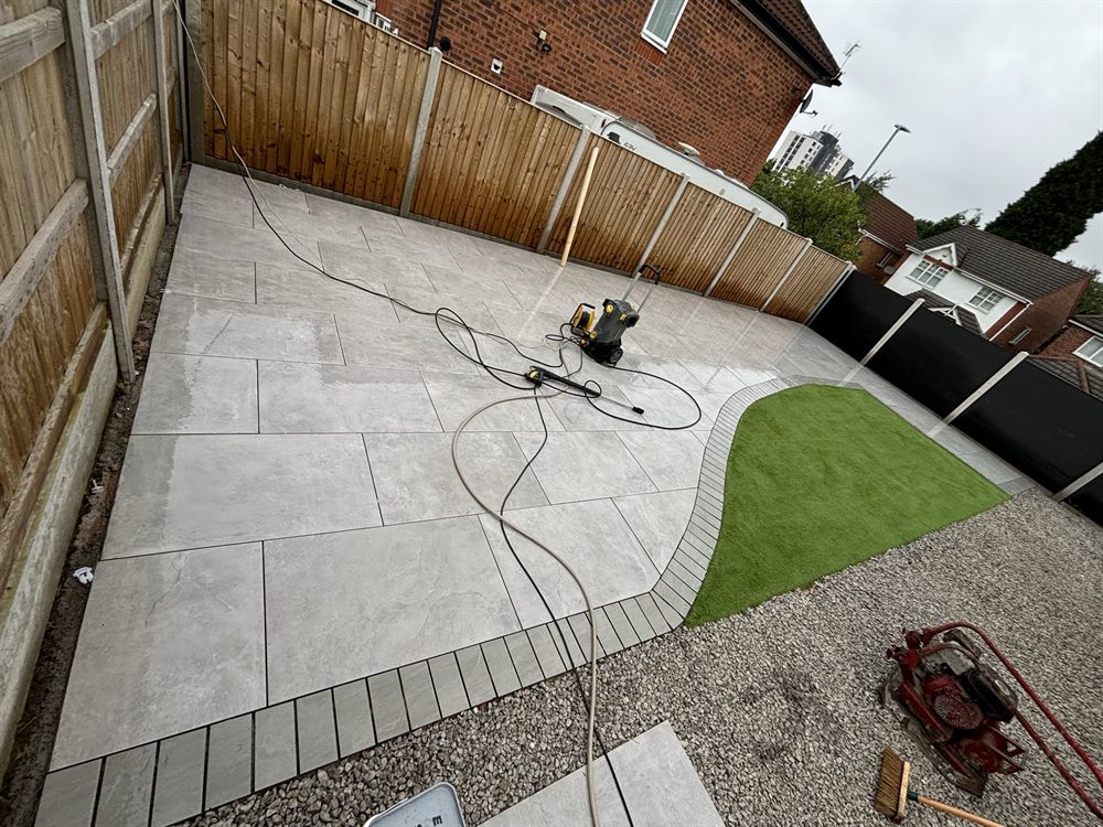 Grey porcelain patio with a curved artificial grass lawn and a gravel border.